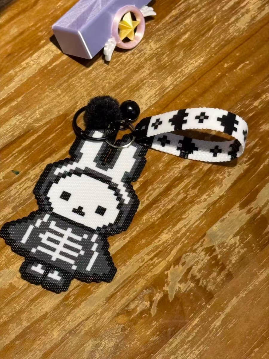 Hand-fused perler bead skeleton bunny keychain with a bell and a black-and-white beaded wrist strap