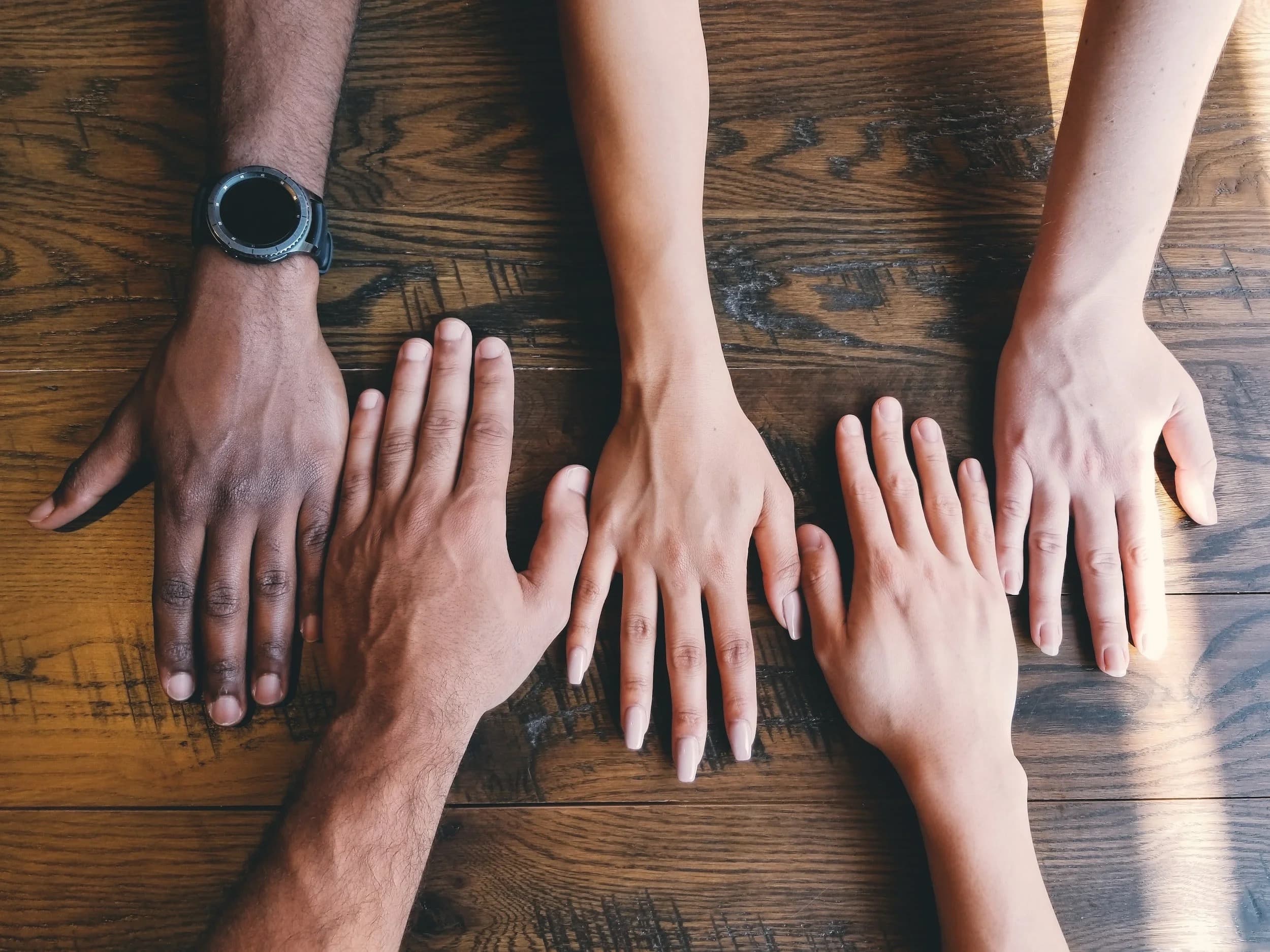 A circle of hands meeting over a wooden table for team bonding